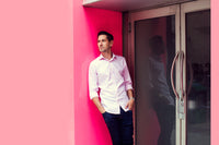 A man in a pink shirt leans against a matching pink wall,